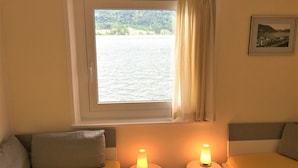 Una habitación con una cama, dos mesitas de noche con lámparas, una ventana con vista a un lago y un cuadro en la pared.