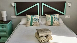 A neatly made bed with two pillows, a bedside table with a lamp, and a green dresser.