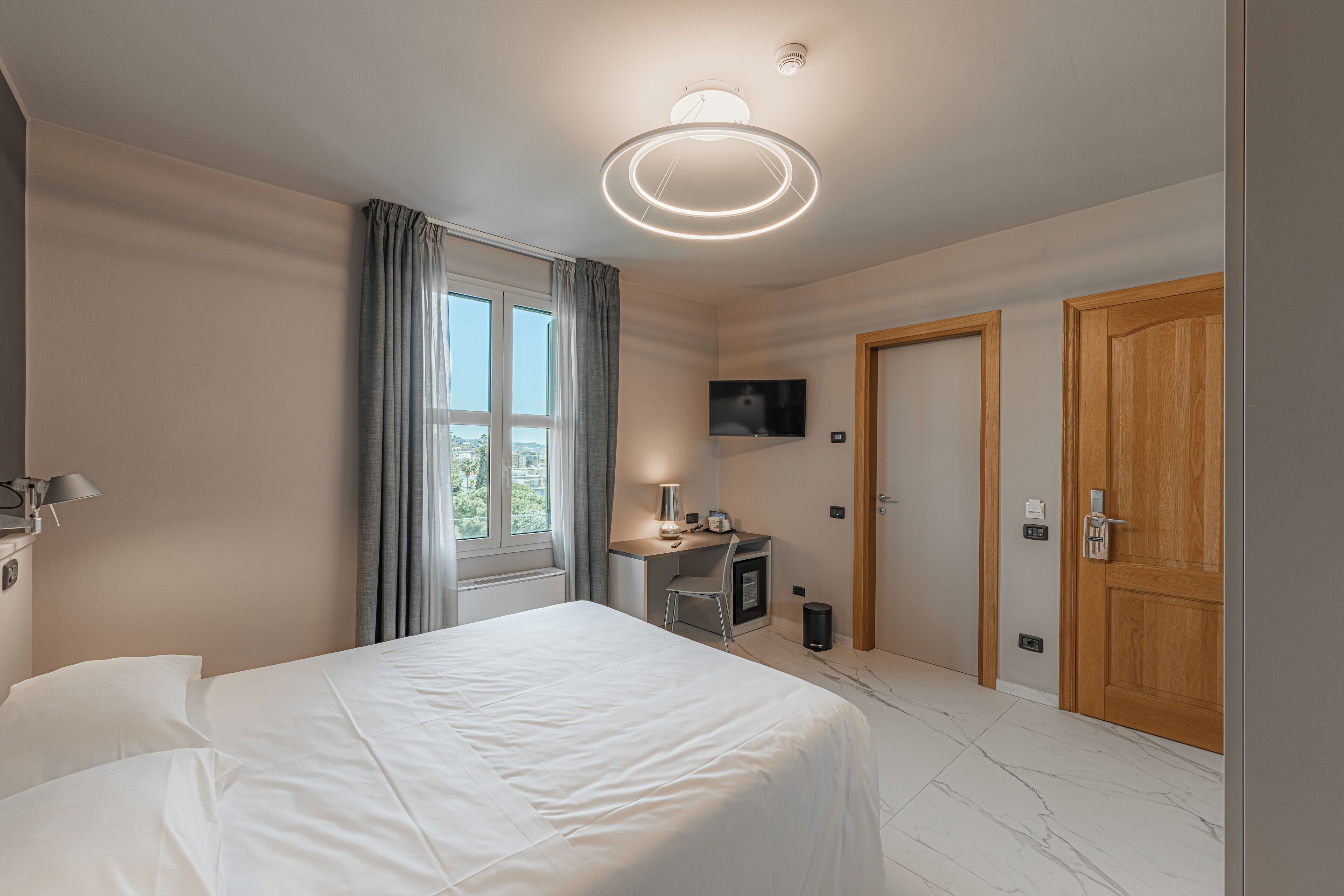 Ein modernes Hotelzimmer mit einem großen Bett, einem Schreibtisch mit Stuhl, einem Fernseher und einer Holztür.
