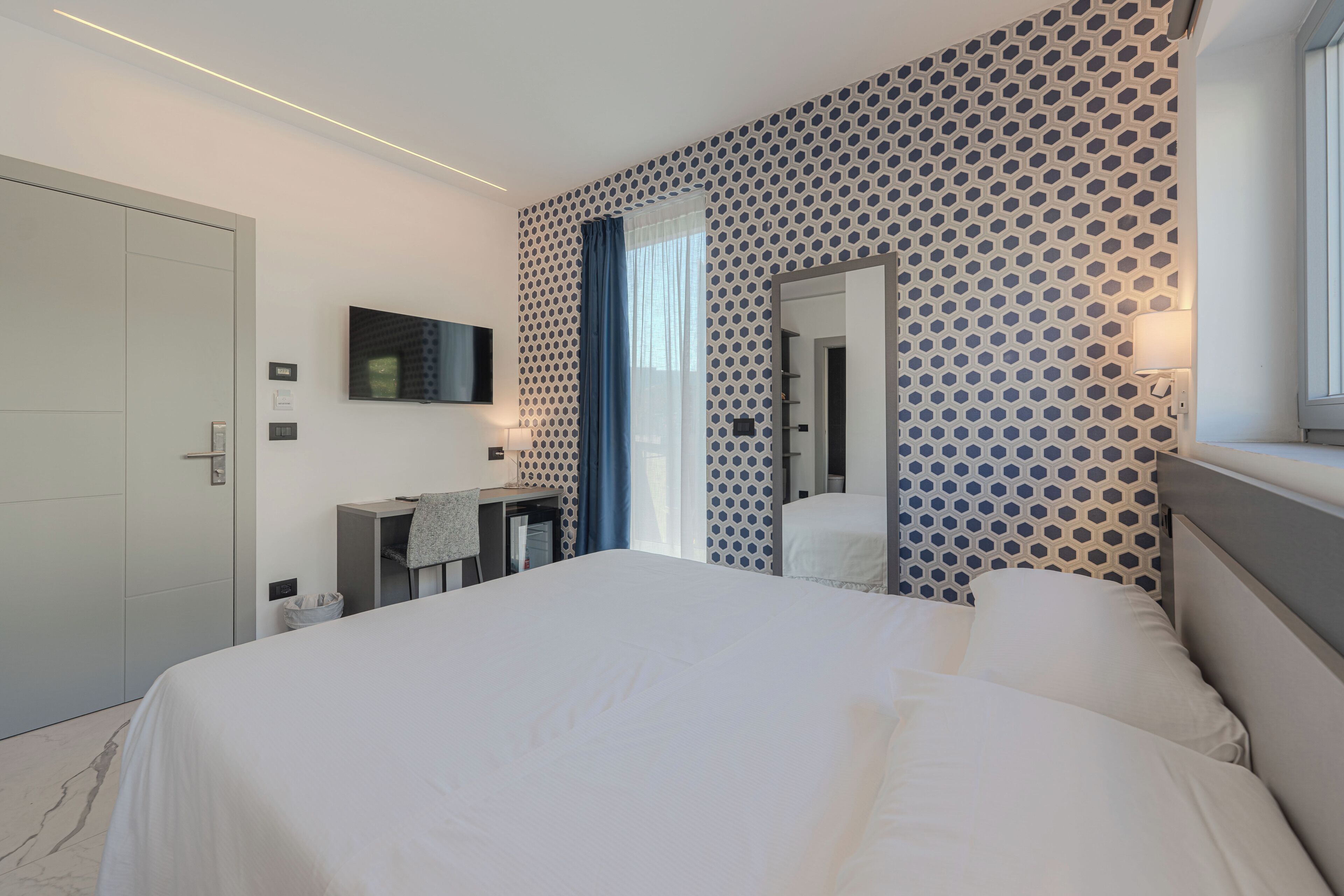 Camera d'albergo moderna con un grande letto, una scrivania, uno specchio e una parete decorata.