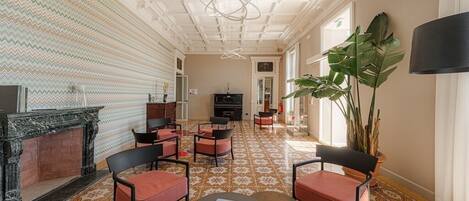 A spacious hallway with patterned flooring, a fireplace, seating area with chairs, and a large plant.