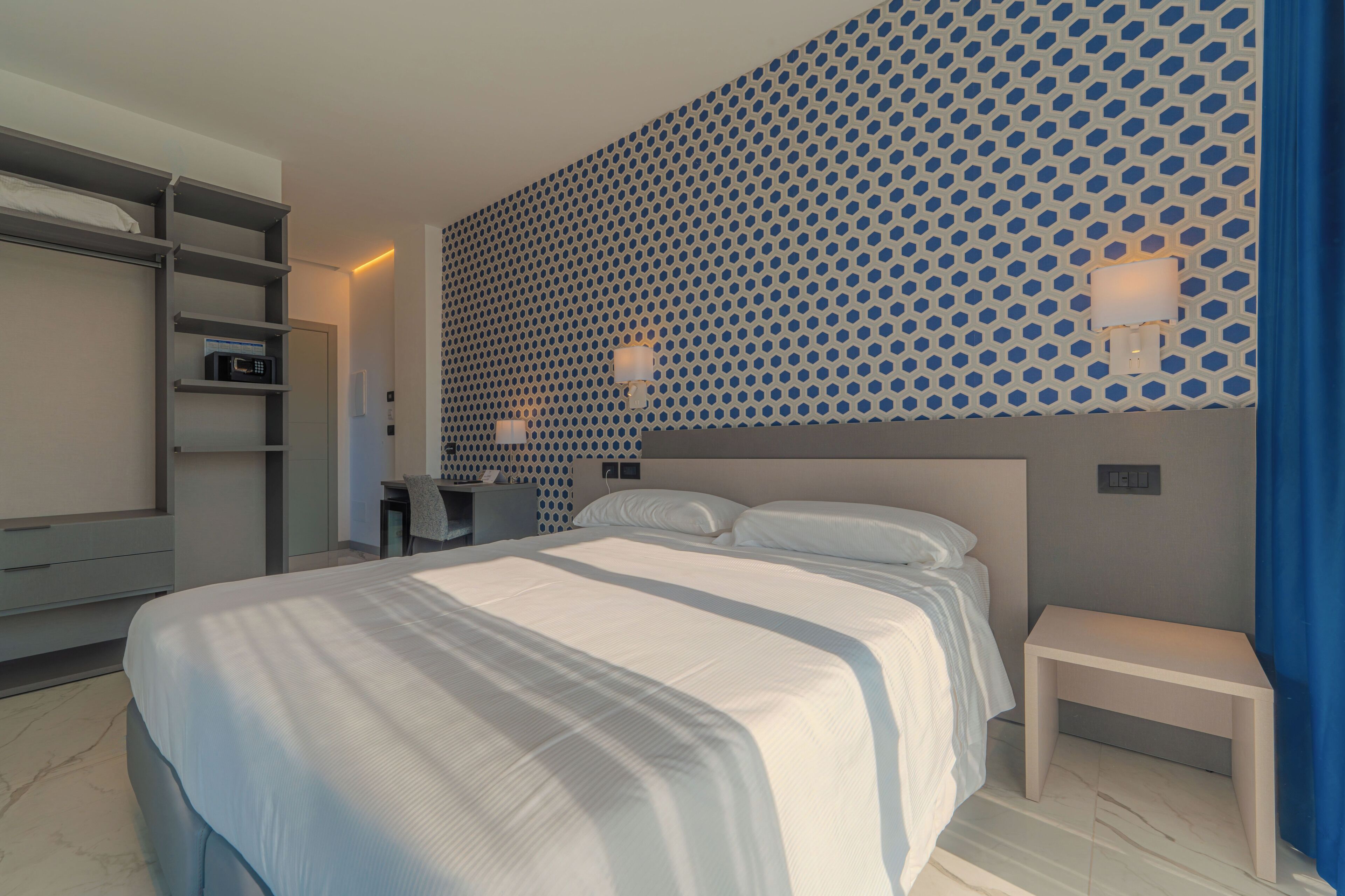 Une chambre d’hôtel moderne, dotée d’un grand lit, d’un bureau et d’un mur orné d’un motif géométrique.