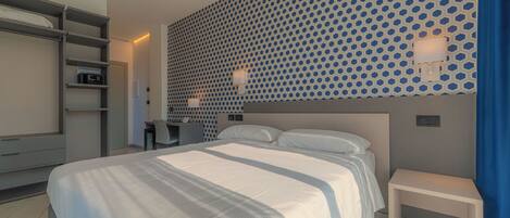 A modern hotel room with a large bed, a desk, and a wall with a geometric pattern.
