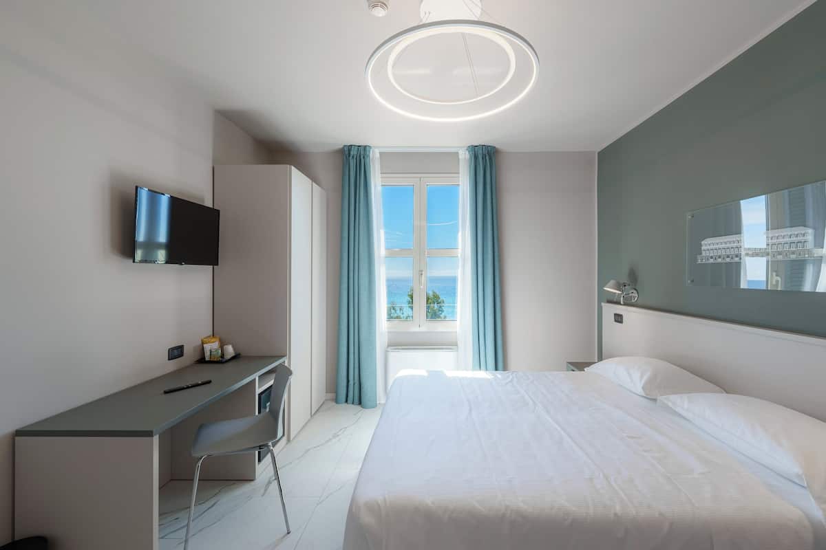 A modern hotel room with a bed, desk, chair, and a TV.