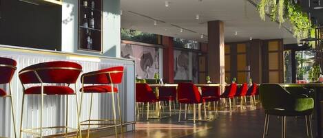 A modern bar area with red and green bar stools, a white counter, and a variety of bottles on shelves.