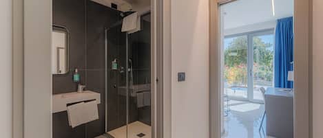 Un baño moderno con ducha envuelta en vidrio, tocador con espejo y vistas al balcón exterior.