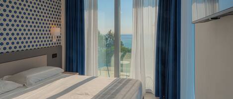 A hotel room with a bed, a patterned wall, a view of the outdoors, and a TV on the wall.