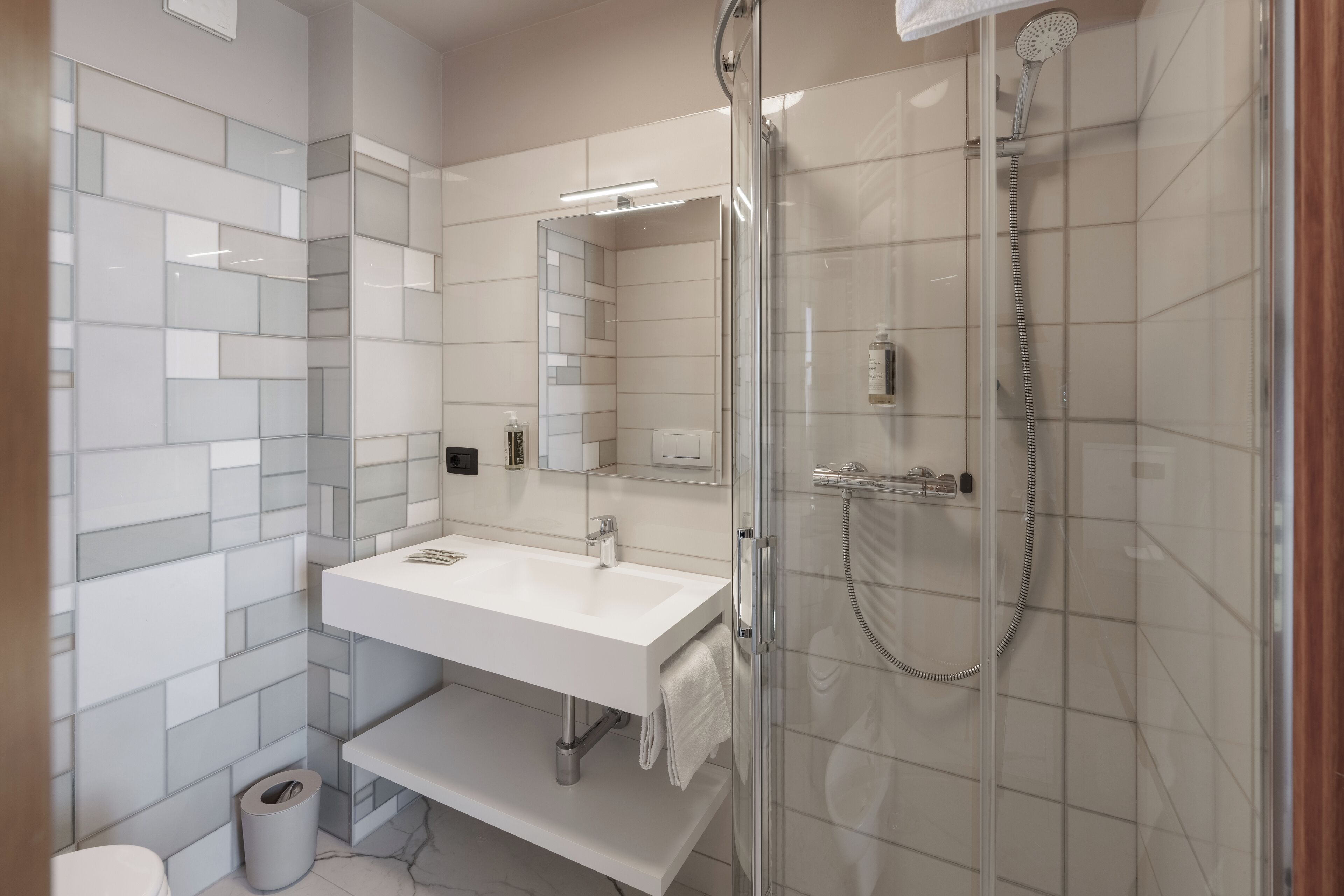 A modern bathroom with a glass-enclosed shower, a white sink, and a mirror above it.