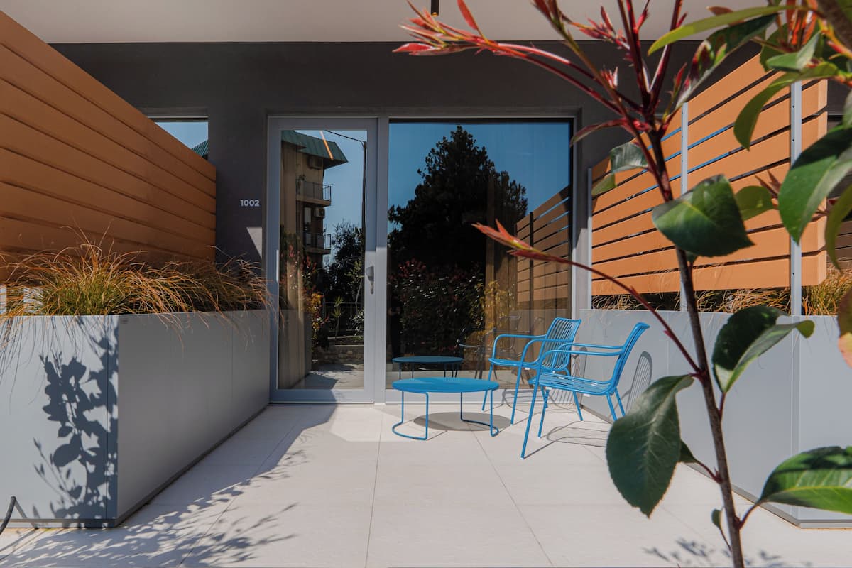 A modern building with a flat roof, a door with a number, and a patio with chairs and tables.