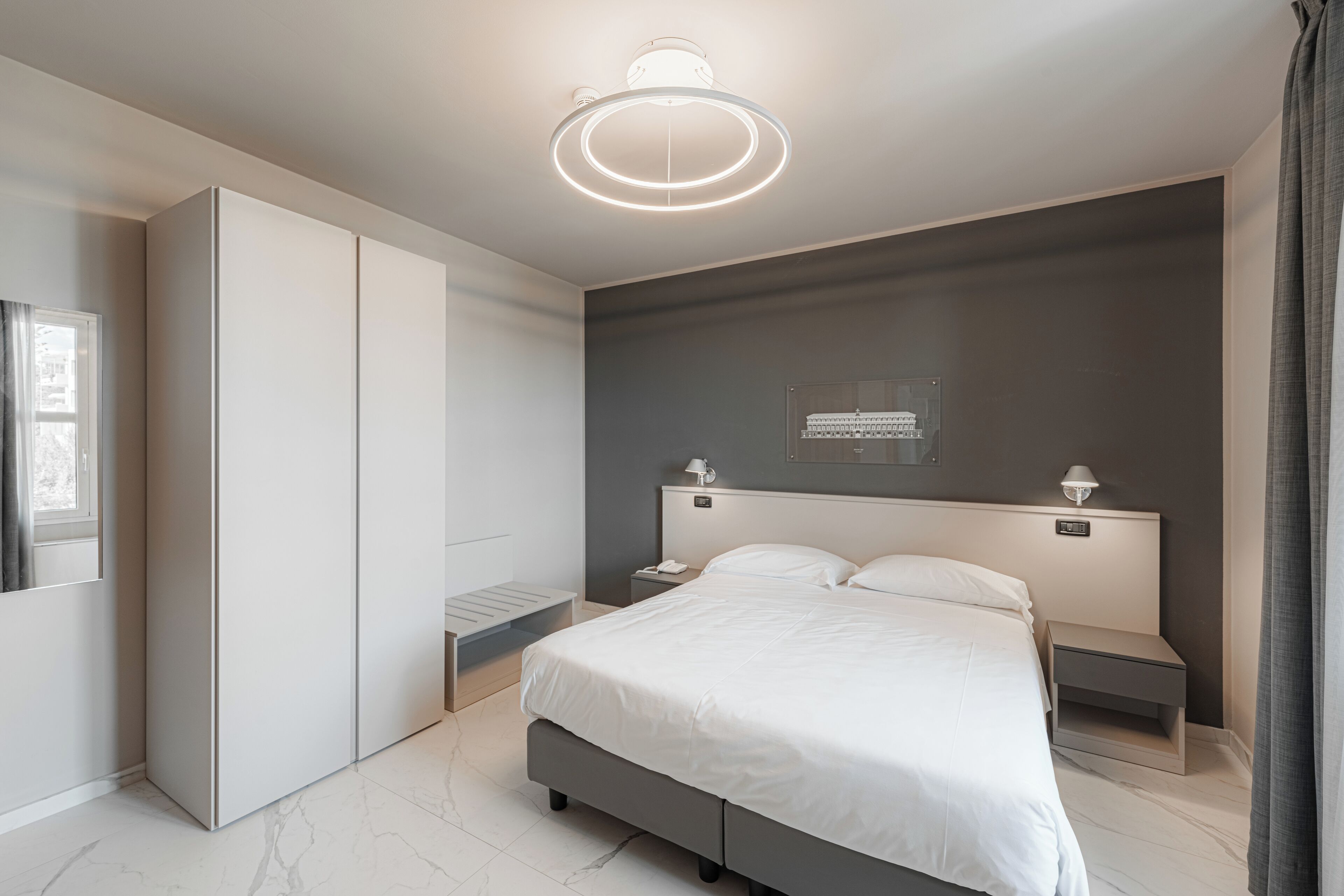 A modern bedroom with a large bed, bedside tables, a wardrobe, and a ceiling light fixture.