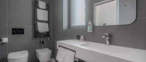 A modern bathroom with a white sink, bidet, and toilet, a towel rack, and a mirror.