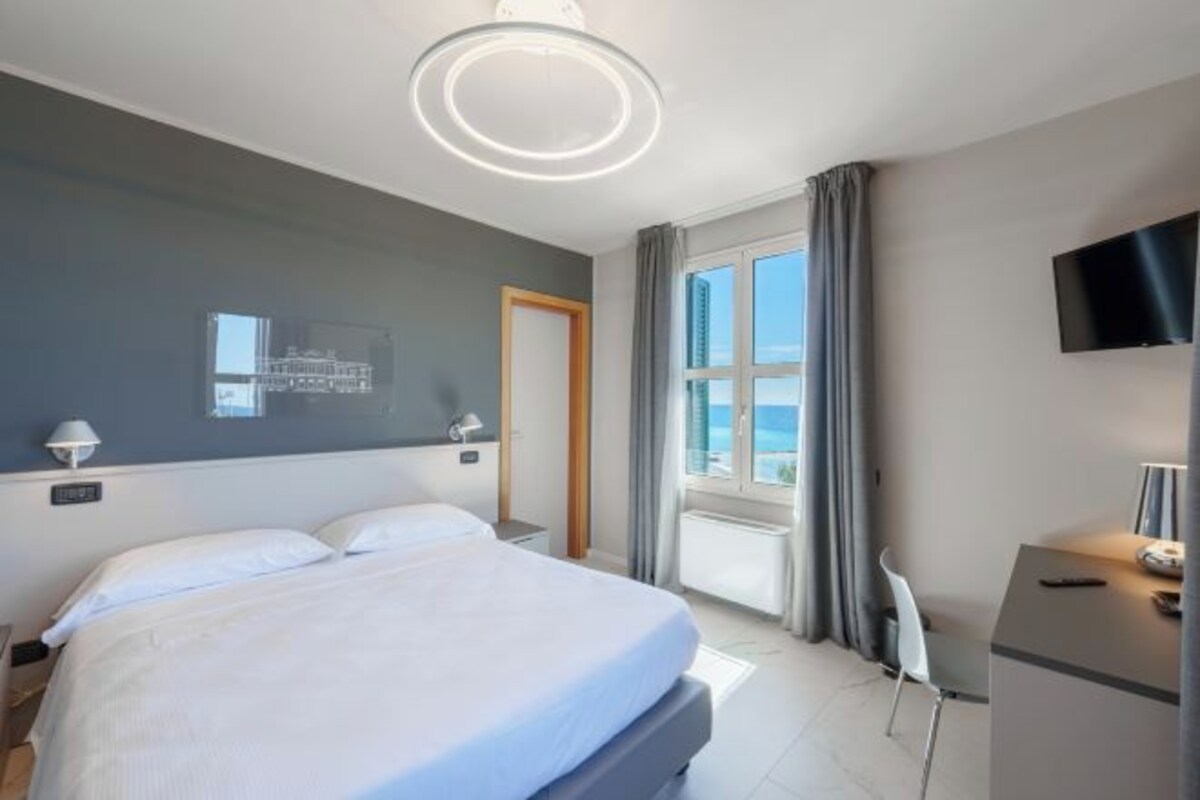A modern hotel room with a large bed, a desk, a chair, a TV, and a window with curtains.