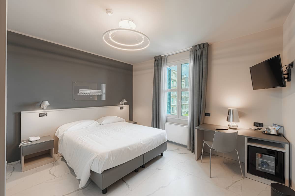 A modern hotel room with a bed, desk, chair, and a TV mounted on the wall.