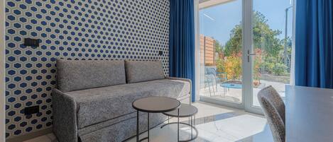 Una habitación moderna con un sofá gris, dos mesas redondas y un ventanal con cortinas azules.