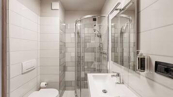 Un baño moderno con ducha de vidrio, lavamanos blanco y inodoro.