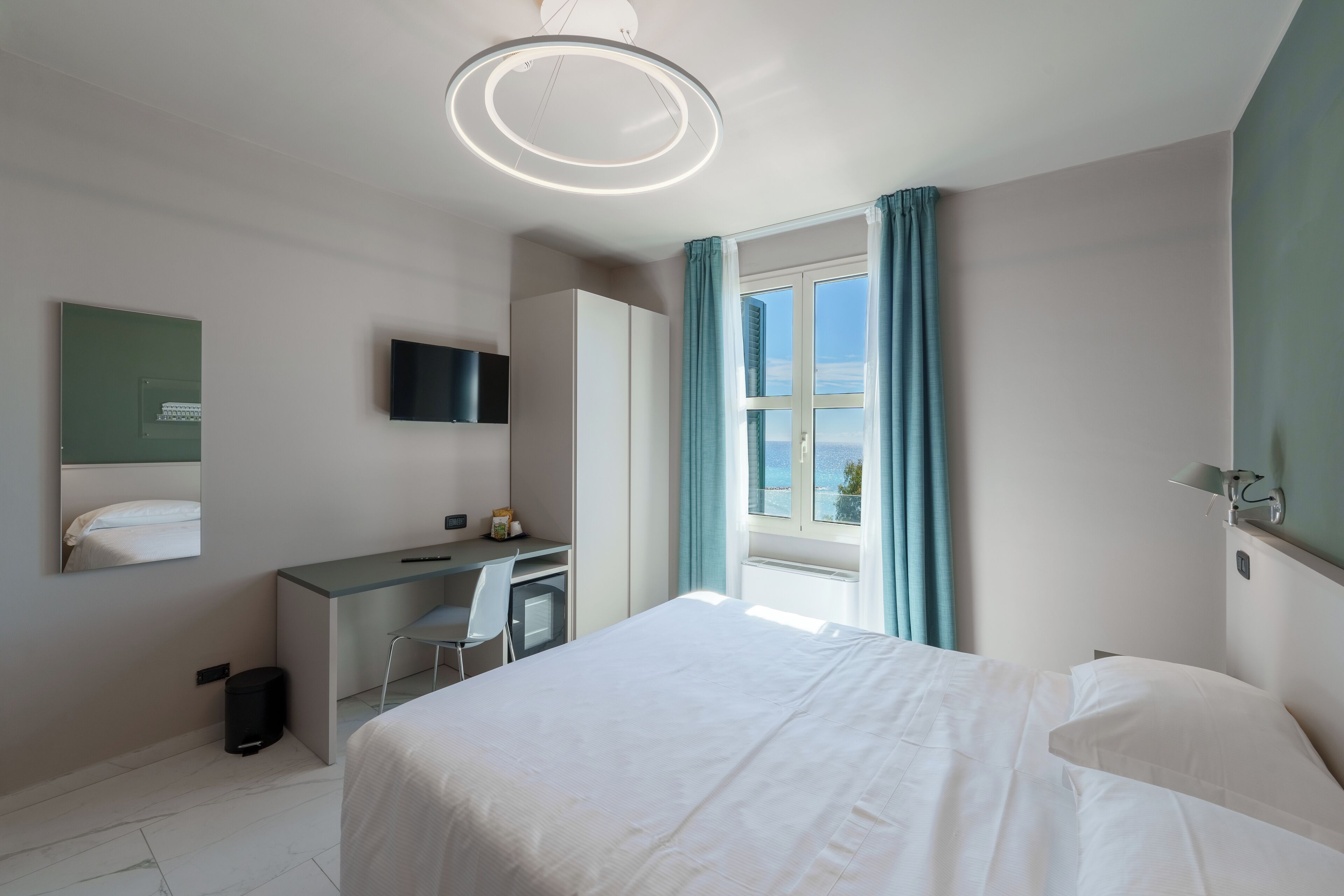 Una habitación de hotel moderna con cama, escritorio, silla, televisor y ventana con cortinas.