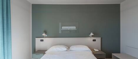 A modern bedroom with a bed, bedside tables, and a wall-mounted light fixture.