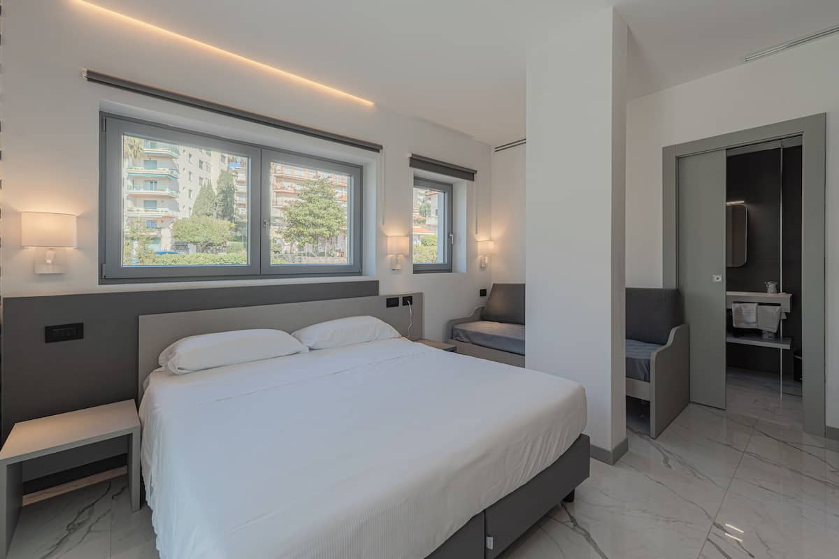 A modern bedroom with a large bed, bedside tables, a bench, and a view of the outside.