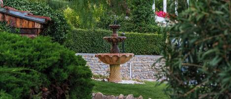 A garden with a central fountain, surrounded by well-maintained hedges and a stone wall.