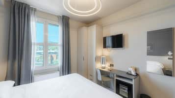 Quarto de hotel com cama, escrivaninha, cadeira, televisão e espelho.