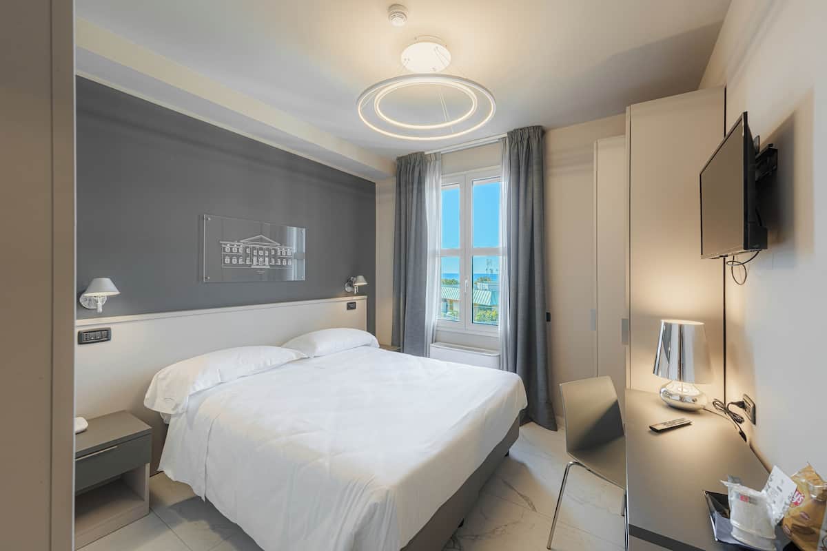 A modern hotel room with a large bed, a desk with a lamp, a TV, and a window with curtains.