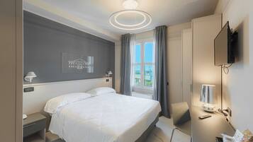 Una habitación de hotel moderna con una cama grande, un escritorio con lámpara, un televisor y una ventana con cortinas.