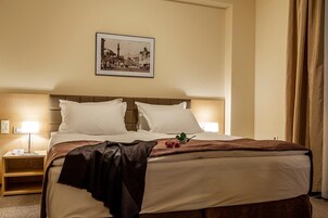 Una habitación de hotel con una cama, una mesita de noche, una lámpara y un cuadro en la pared.