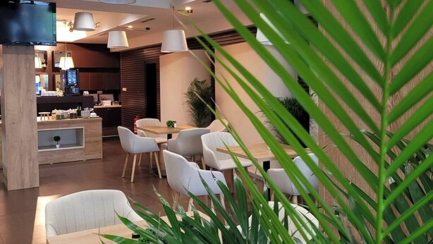 Uma sala de jantar moderna com cadeiras e mesas brancas, iluminação pendente e um vaso grande em primeiro plano.