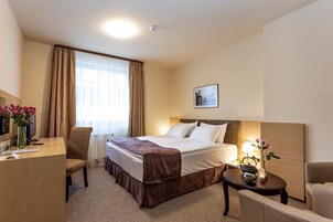Una habitación de hotel con cama, escritorio, silla, mesita de noche y lámpara.