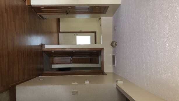 A room with a kitchenette area, wooden cabinets, a countertop, and a door leading to another room.