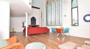 A spacious living area with a red sofa, a glass dining table with chairs, and large windows with stained glass. - 6 Rose Chapel Penthouse (Truro)