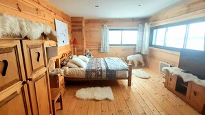 Une pièce aménagée comme un chalet en bois, avec un lit, une chaise, une commode et une fenêtre avec des rideaux.