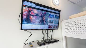 Un televisor de pantalla plana montado en la pared muestra un video de YouTube. Debajo del televisor, hay un estante blanco con un control remoto y un dispositivo electrónico negro.