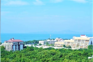 Paisagem costeira urbana com um hotel de destaque, com vários andares e varandas, rodeado por vegetação exuberante e vista clara para o mar.