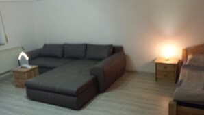 A modern living room with a sectional sofa, a small side table, and a bedside table with a lamp. - Monteurzimmer & Ferienwohnung G. Klement (Herrieden)