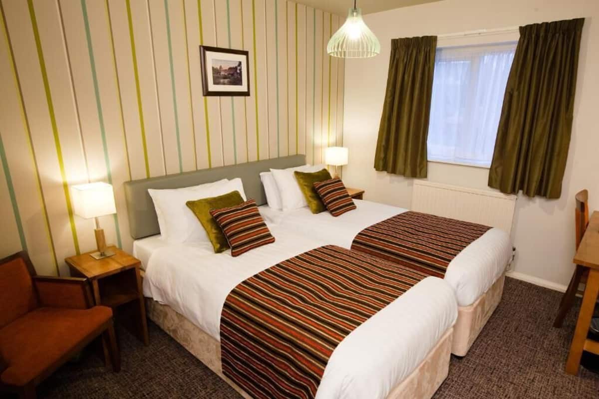 A double bed with striped bedding, two bedside tables with lamps, a framed picture on the wall, and a window with curtains.
