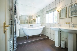 Un baño moderno con una bañera independiente, un lavabo pedestal y un espejo grande.