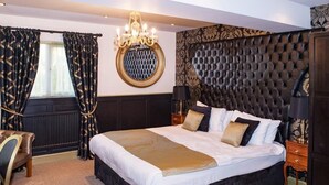 A bedroom with a large bed, a round mirror, a tufted headboard, a chandelier, and a dark-colored wardrobe. - Henley Hotel (Henley-in-Arden)