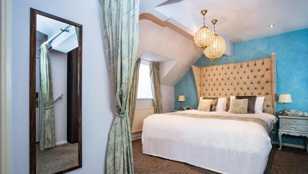 Een slaapkamer met een groot bed, een spiegel, een kroonluchter en een blauwe accentmuur.