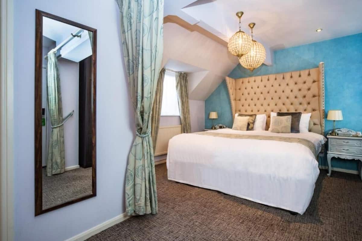 A bedroom with a large bed, a mirror, a chandelier, and a blue accent wall.