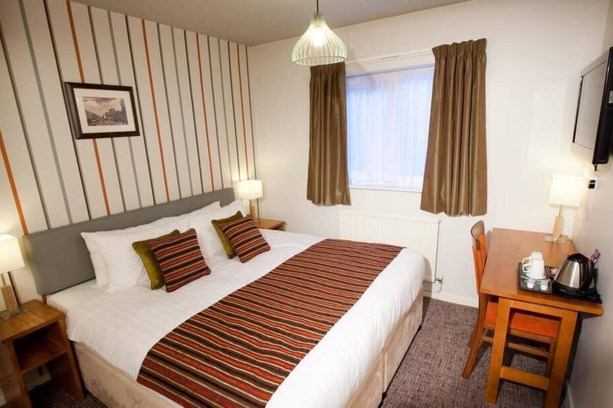 A hotel room with a bed, bedside tables, a desk, and a window with curtains.