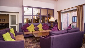A living room with purple sofas, a coffee table, and a large window with curtains. - Henley Hotel (Henley-in-Arden)