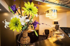 Un comedor con una mesa dispuesta para dos personas, un jarrón de flores y una araña.