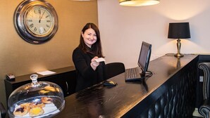 A reception desk with a clock, a laptop, and a coffee station. - Henley Hotel (Henley-in-Arden)