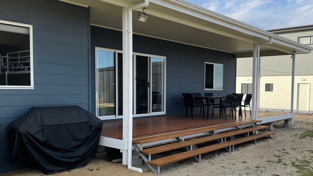 Eine überdachte Terrasse mit Holzdeck, Grill und Tisch mit Stühlen.