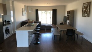 Eine moderne Küche mit einer zentralen Kochinsel, Barhocker, einem Esstisch mit Stühlen, einer Couch und einem Fernseher auf einem Schrank.