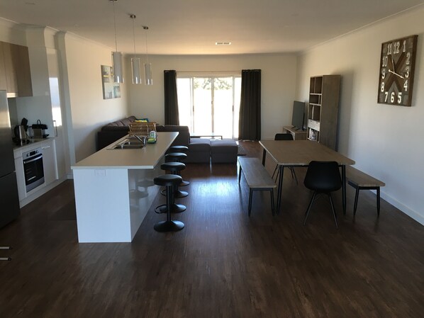 Een moderne keuken met een centraal eiland, barstoelen, een eettafel met stoelen, een bank en een televisie op een dressoir.