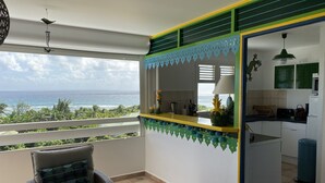 A balcony with a view of the ocean, a small kitchen area, and a dining table with chairs. - Magnifique appartement vue mer 180° - Hauteur anse Des Rochers - Avec Cuve Eau (Saint-François)