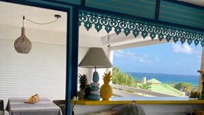 A kitchen with a washing machine, a dining area with a table and chairs, and a view of the ocean. - Magnifique appartement vue mer 180° - Hauteur anse Des Rochers - Avec Cuve Eau (Saint-François)