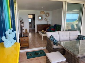 A living room with a sofa, a glass-top table, and a view of the ocean.